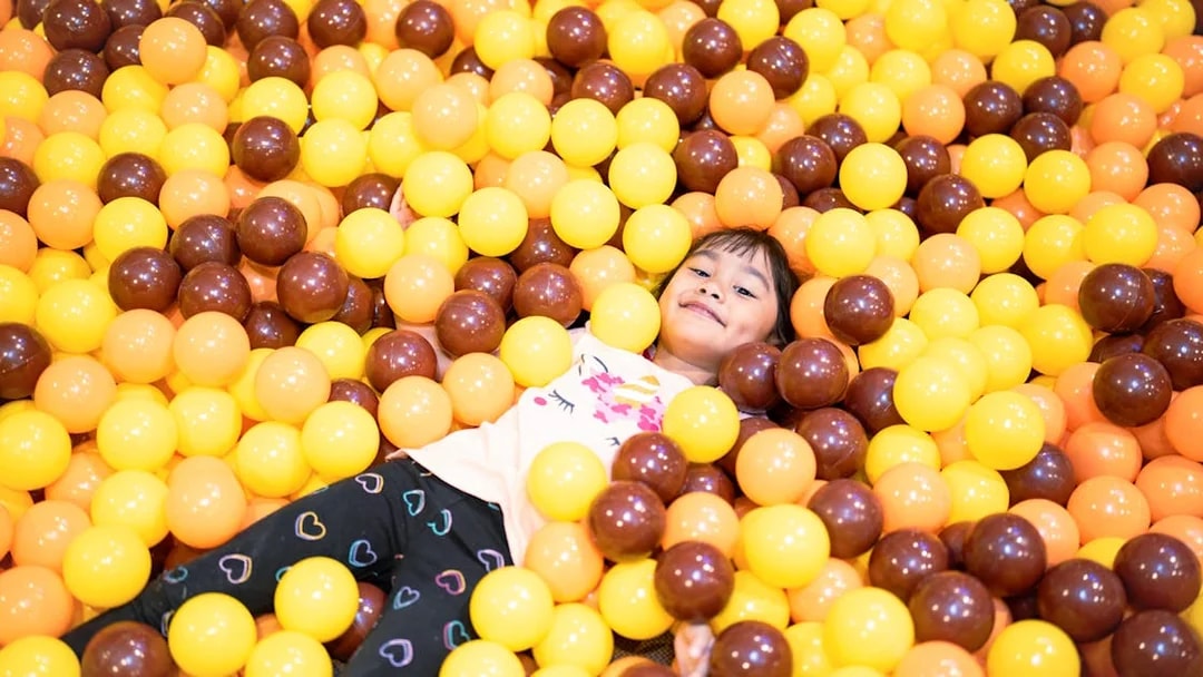 Child playing in a ball pit filled with yellow and brown balls.