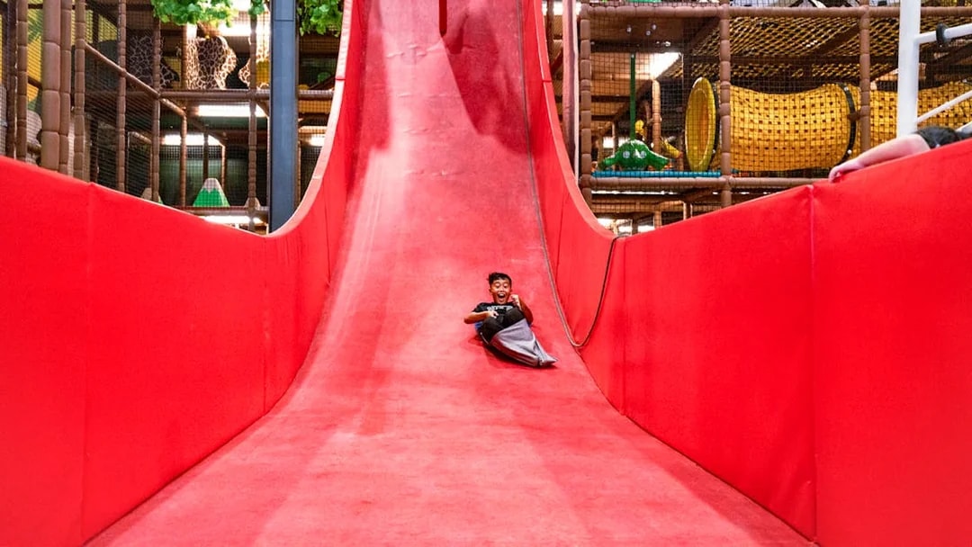 Child enjoying a ride down a large red slide in an indoor play area.