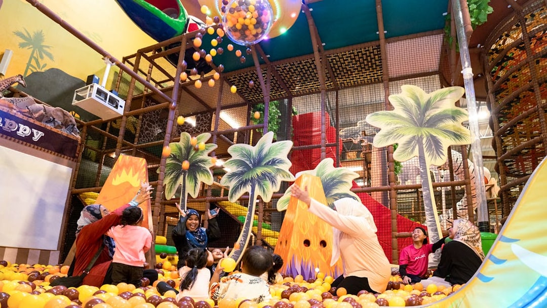 Children playing in a colorful ball pit at Safari Escape Playland with palm tree decorations.