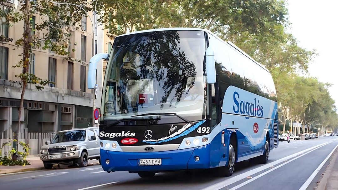 Bus for Girona Airport transfer to Barcelona city center on a tree-lined street.