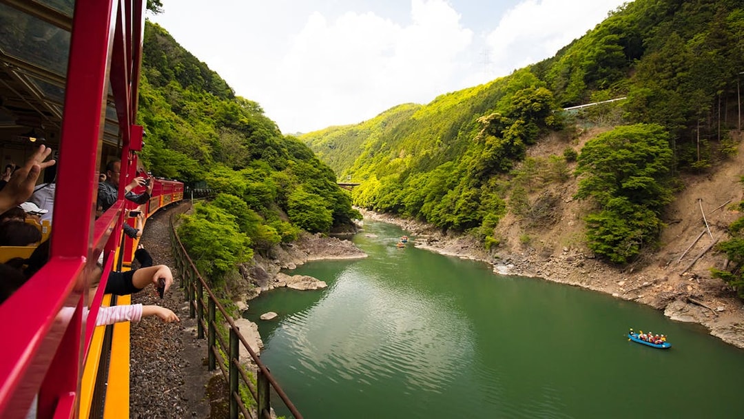 Sagano Romantic Train passing through lush green valley alongside a river in Kyoto, Japan.