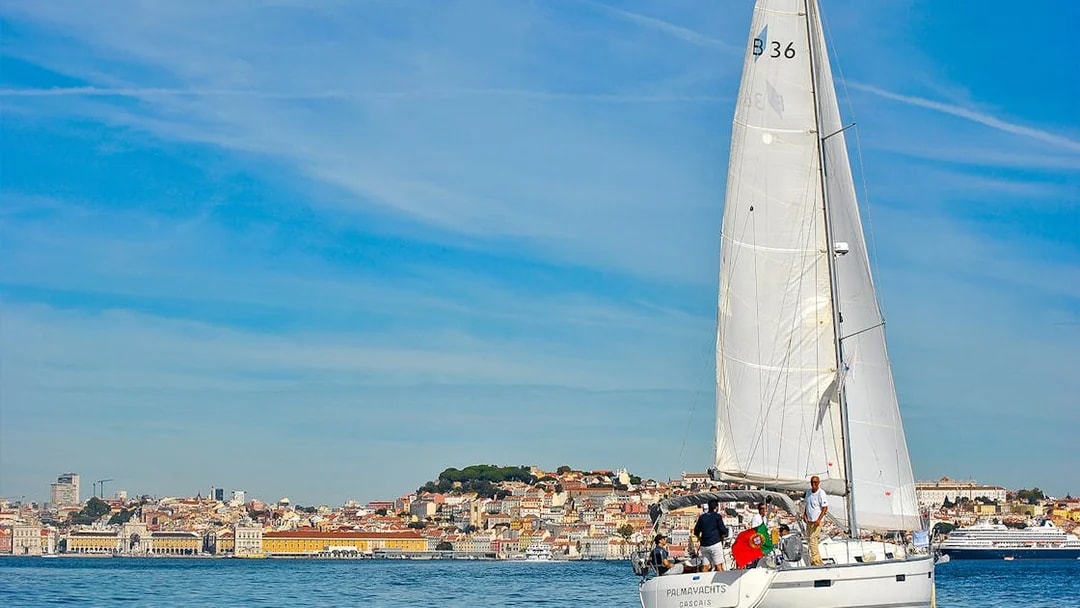 Sailboat on Tagus River with Lisbon cityscape in the background.