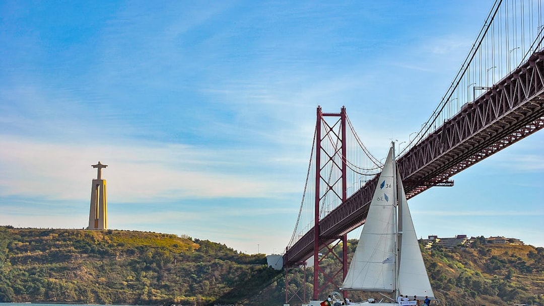 Sailboat on Tagus River near 25 de Abril Bridge and Cristo Rei statue in Lisbon.