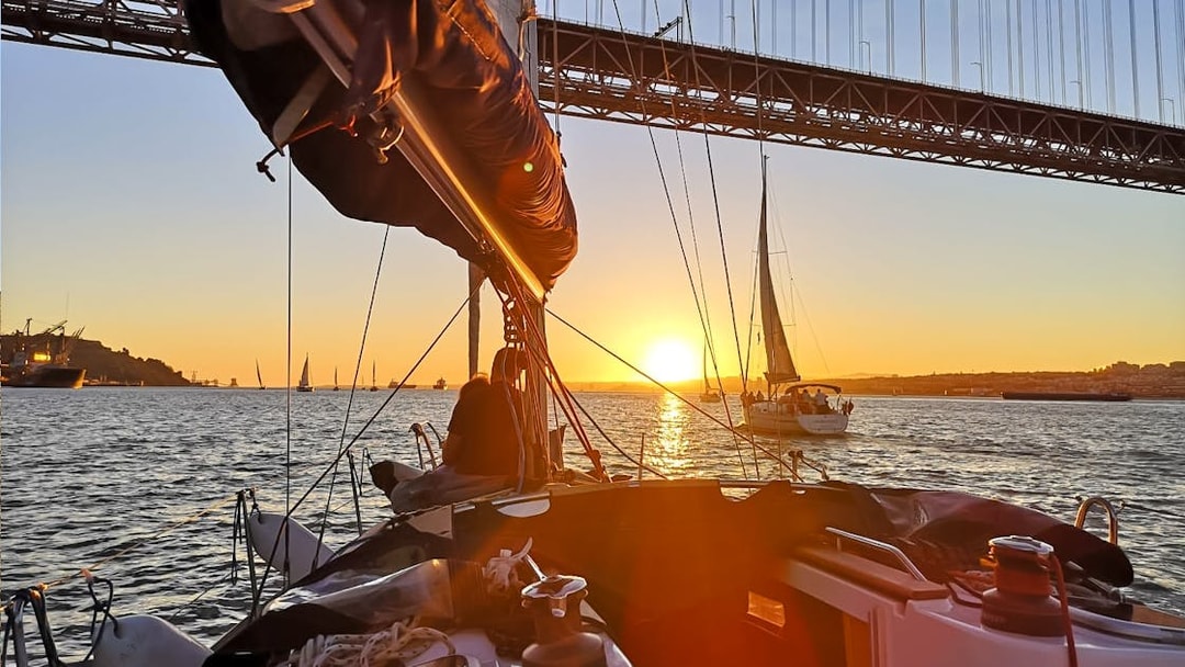 Sailboats on Tagus River at sunset with Lisbon's bridge in view.