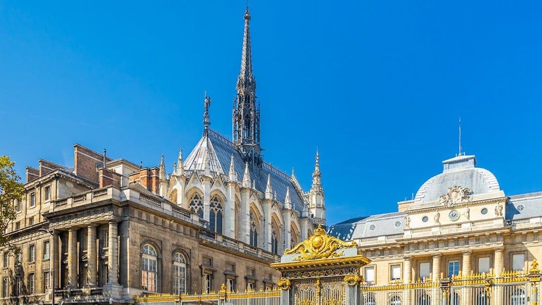 Sainte Chapelle spire and Conciergerie facade in Paris with ornate golden gate.