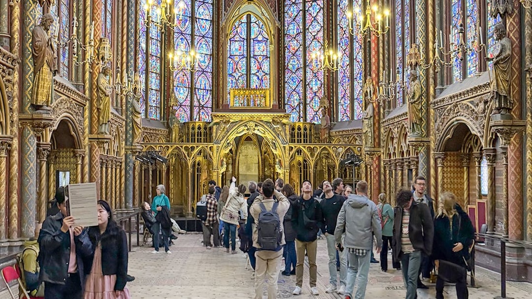 Visitors inside Sainte Chapelle, Paris, admiring stained glass windows and ornate Gothic architecture.