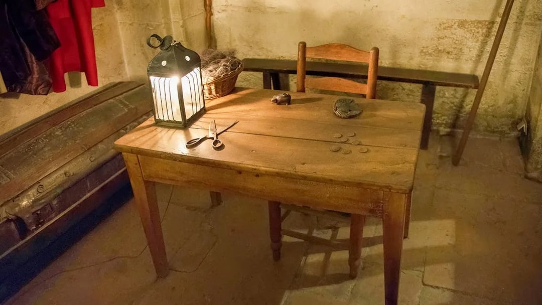 Wooden table with lantern, coins, and scissors in a historic palace room.