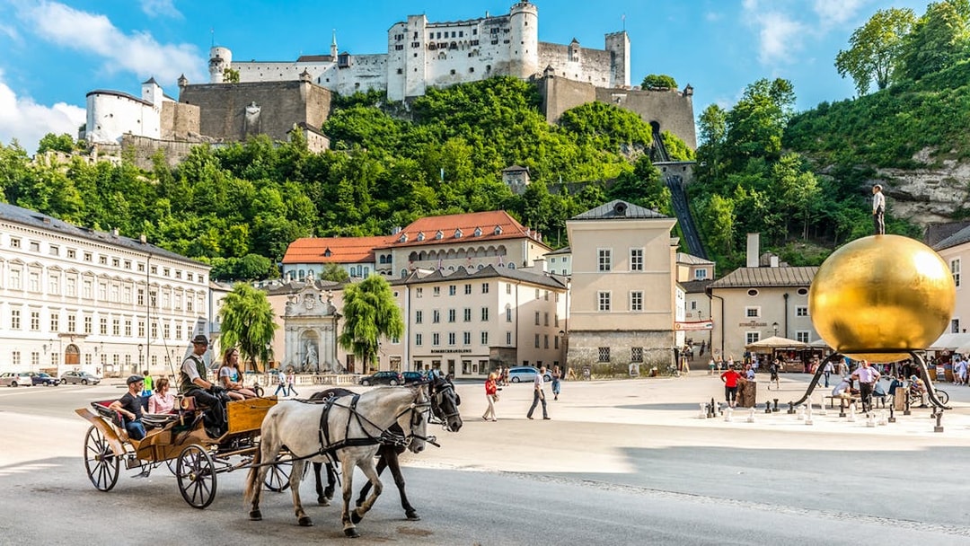Horse-drawn carriage in Salzburg's Kapitelplatz with Hohensalzburg Fortress in the background.