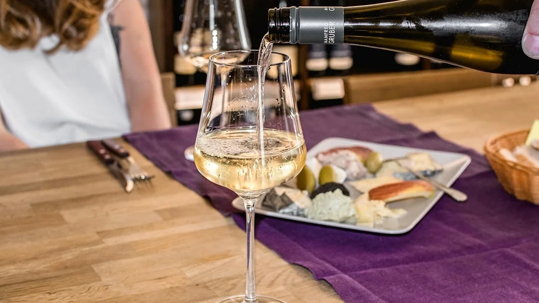 Wine being poured into a glass at a hidden wine bar with a cheese platter nearby.