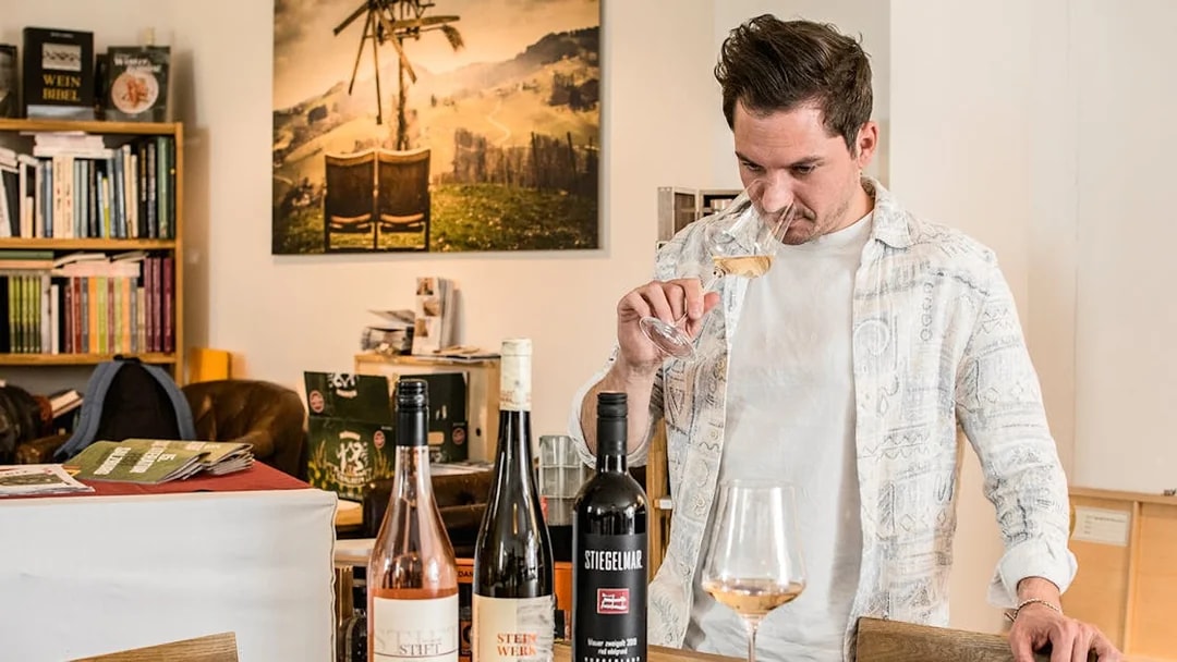 Man tasting wine in a cozy wine bar with bottles on the table.