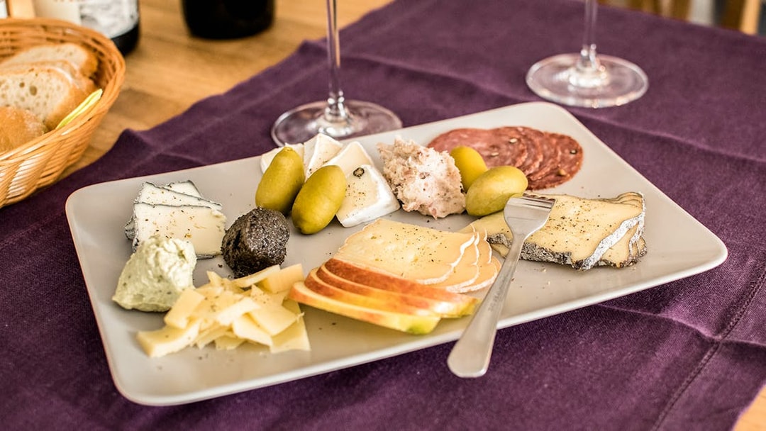 Cheese platter with assorted cheeses, olives, and charcuterie on a table with wine glasses.