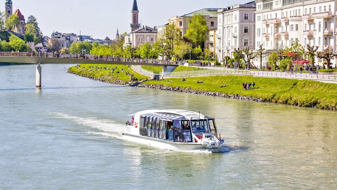 Salzburg river cruise boat on the Salzach River with cityscape and bridge in the background.