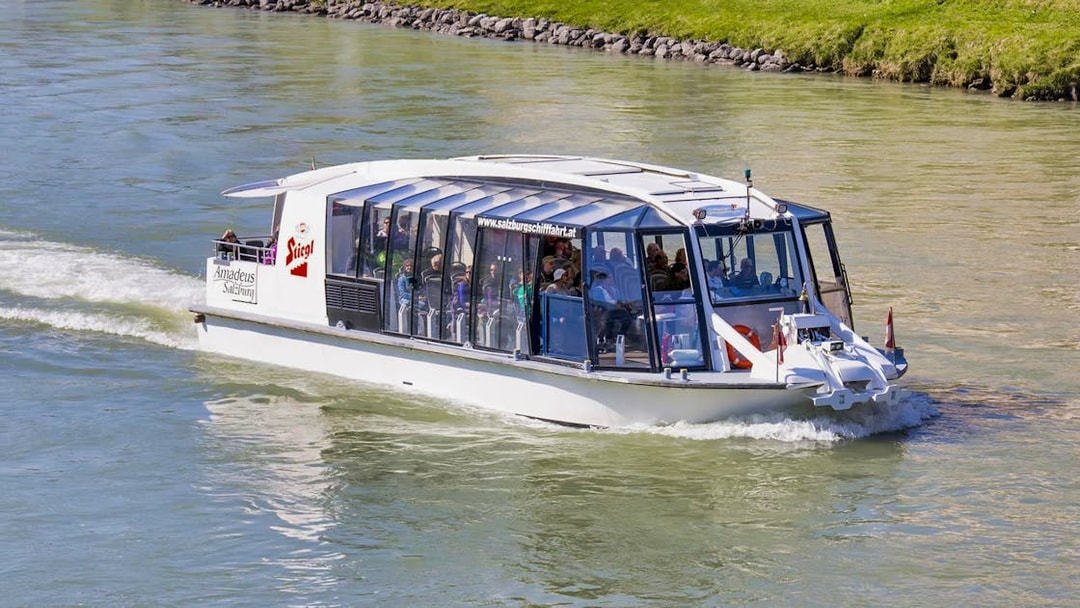 Salzburg river cruise boat on Salzach River with passengers enjoying city views.