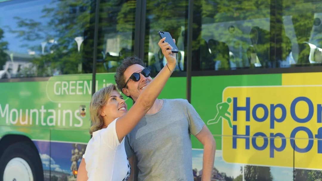 Tourists taking a selfie in front of a Hop On Hop Off bus in Salzburg.