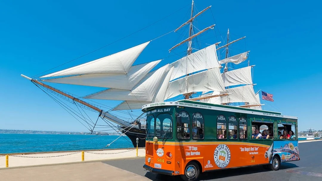 San Diego Old Town Trolley passing a historic sailing ship by the waterfront.