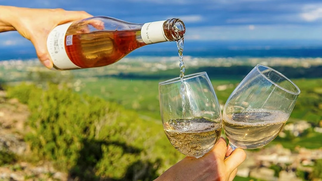 Pouring wine into glasses with Napa Valley landscape in the background.