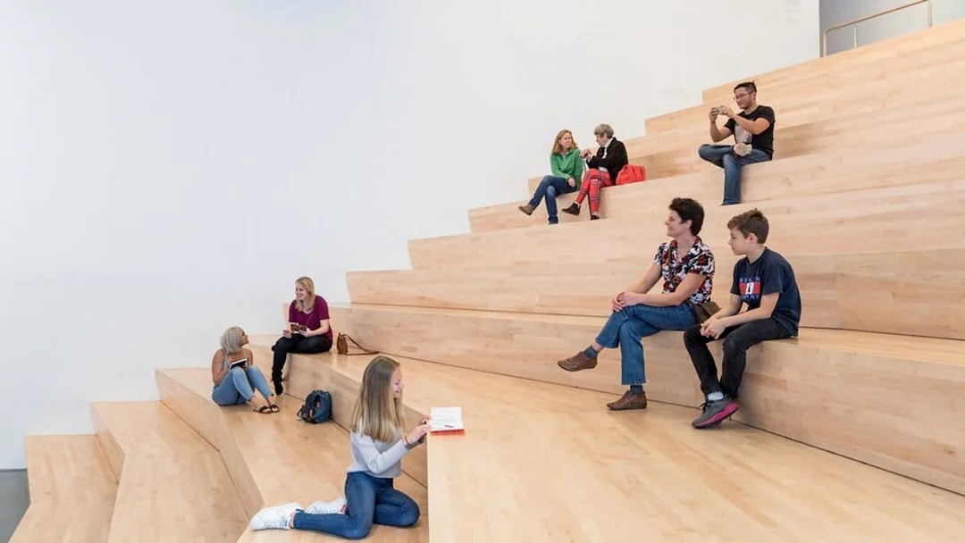 Visitors sitting on wooden steps inside San Francisco Museum of Modern Art.