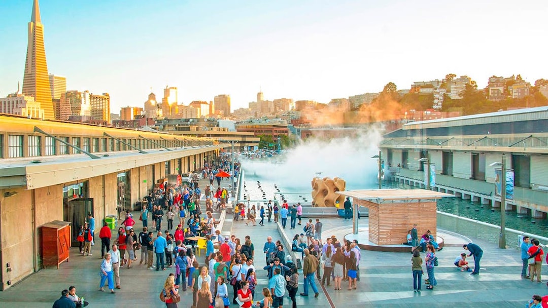 Crowd at San Francisco's Exploratorium with city skyline in background.