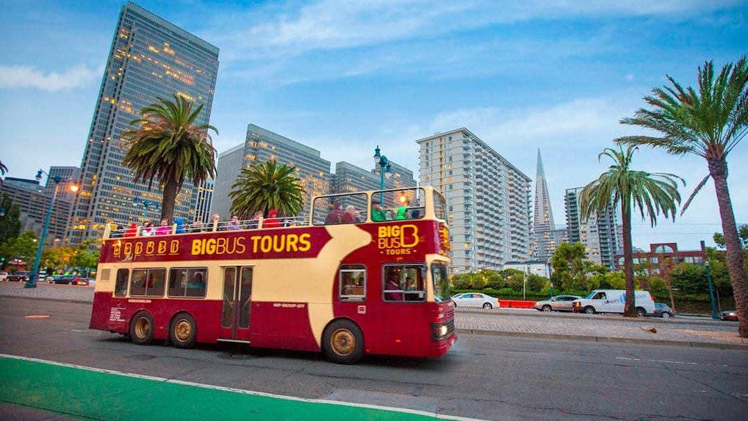 Open-top tour bus in San Francisco with city skyline and palm trees.