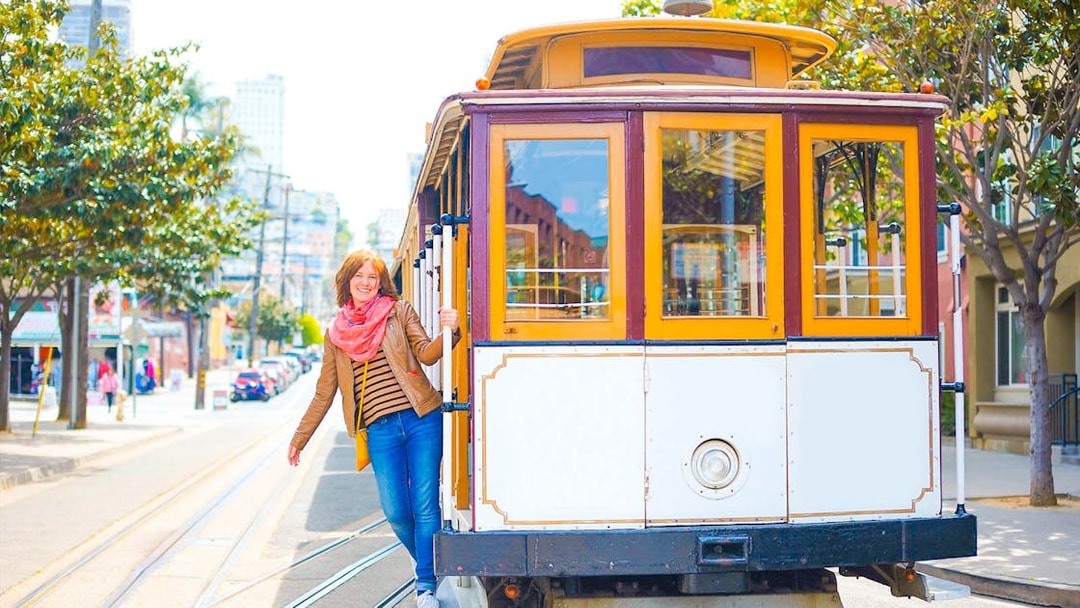 Person riding a San Francisco cable car on a sunny street.