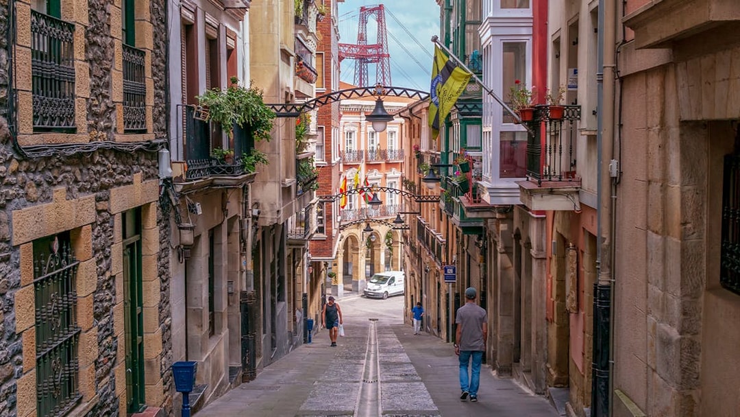 Narrow street in Bilbao with colorful buildings and the Vizcaya Bridge in the background.