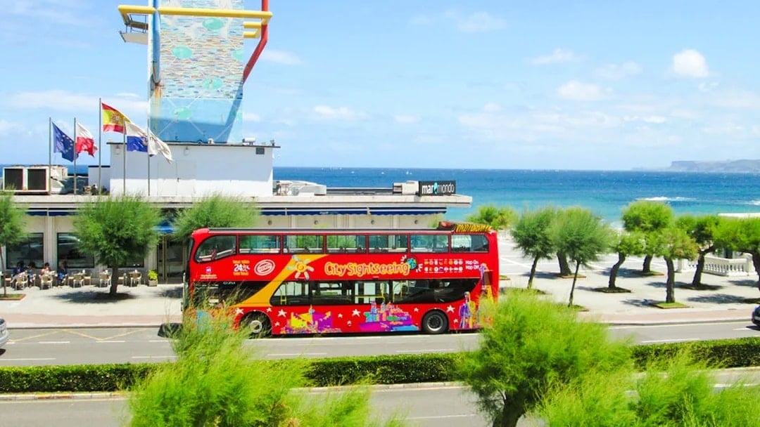 Santander cityscape with red City Sightseeing bus near coastal historic buildings.