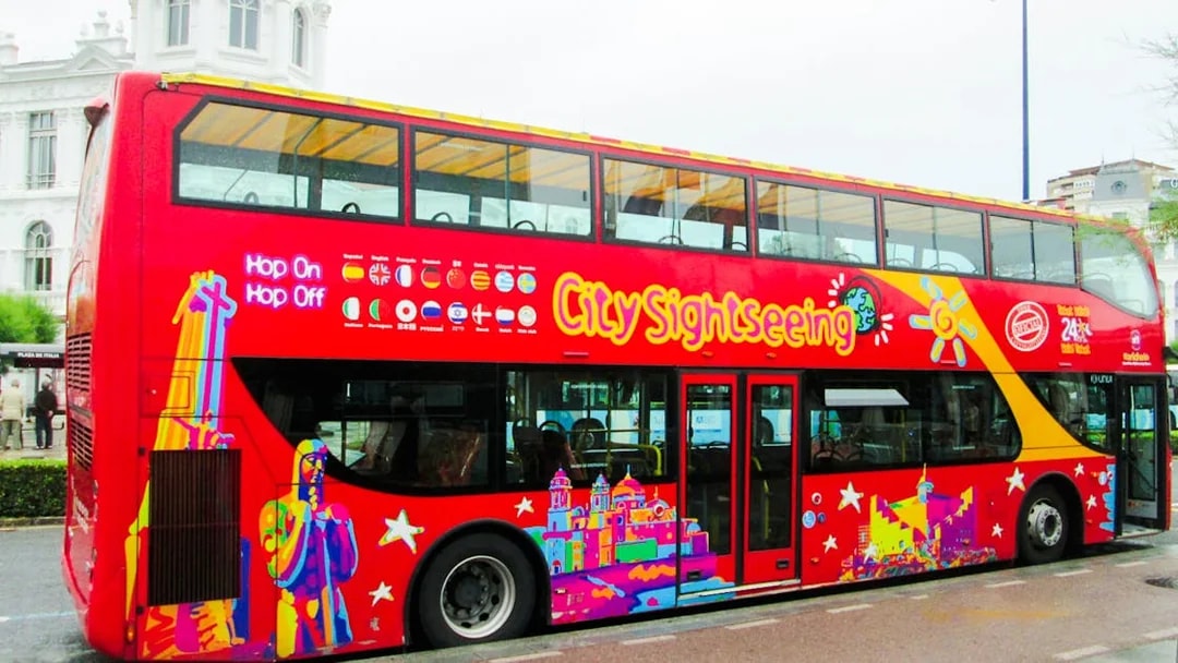 Red double-decker bus for City Sightseeing tour in Santander, parked near a historic building.