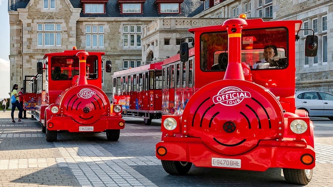 Red sightseeing train parked in front of historic building on panoramic train tour.