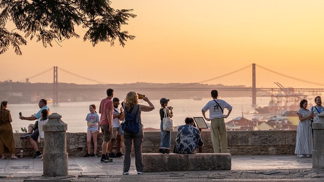 Visitors capturing sunset views from St George's Castle with Lisbon's bridge in the background.