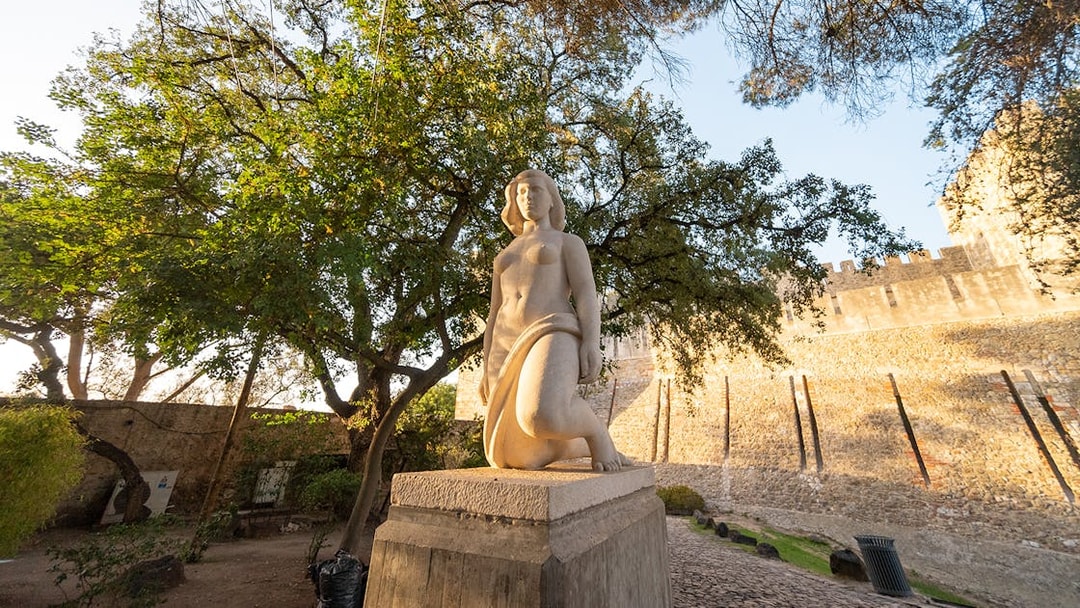 Statue in St George's Castle Gardens with trees and castle wall in Lisbon.