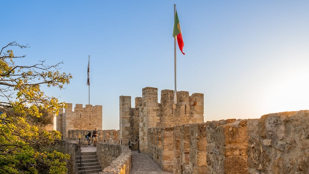 St. George’s Castle walls with Portuguese flag at sunset, Lisbon.