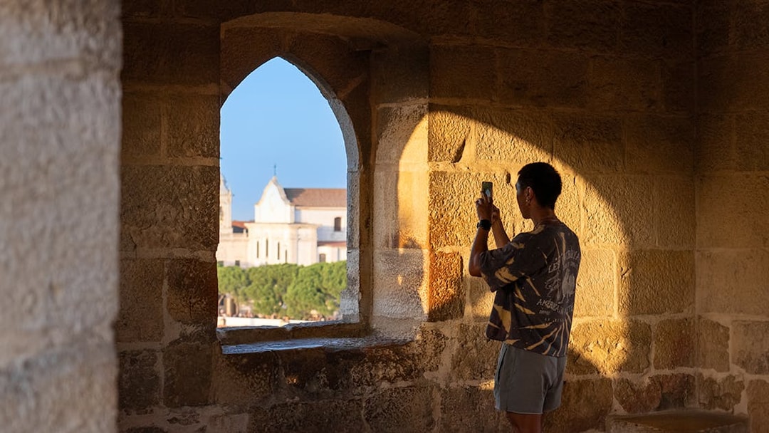 Visitor taking photo of St. George’s Castle through stone archway at sunset.