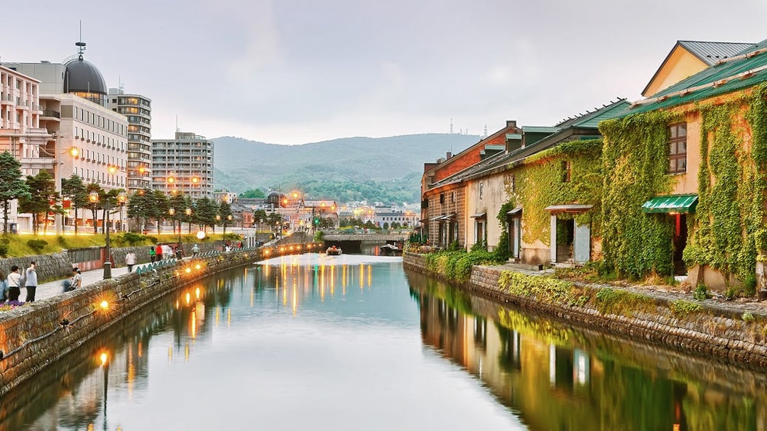 Otaru Canal at dusk with historic warehouses and city lights reflecting on the water.