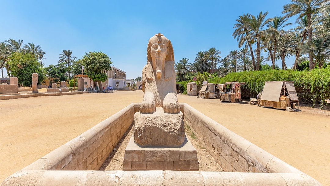 Alabaster sphinx at Memphis, Egypt, surrounded by palm trees and market stalls.