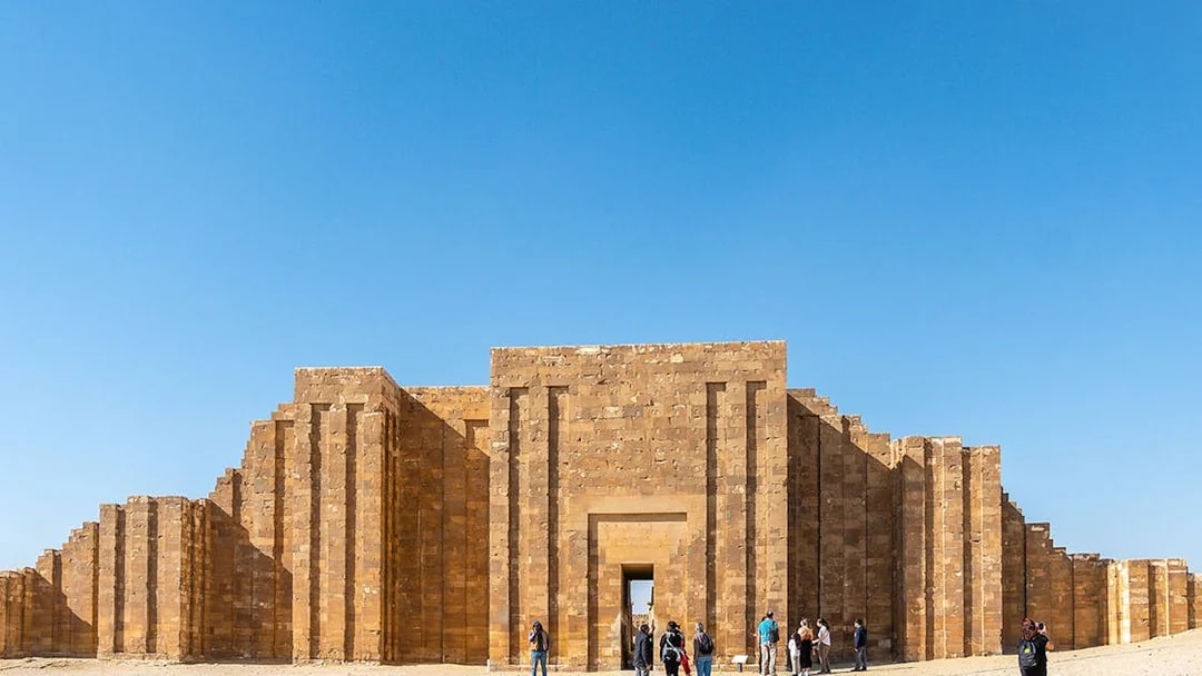Entrance to the Pyramid of Djoser complex in Saqqara, Egypt, with visitors exploring.