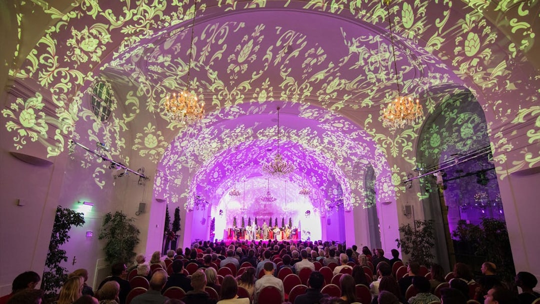 Concert audience in Schönbrunn Palace with ornate ceiling projections.