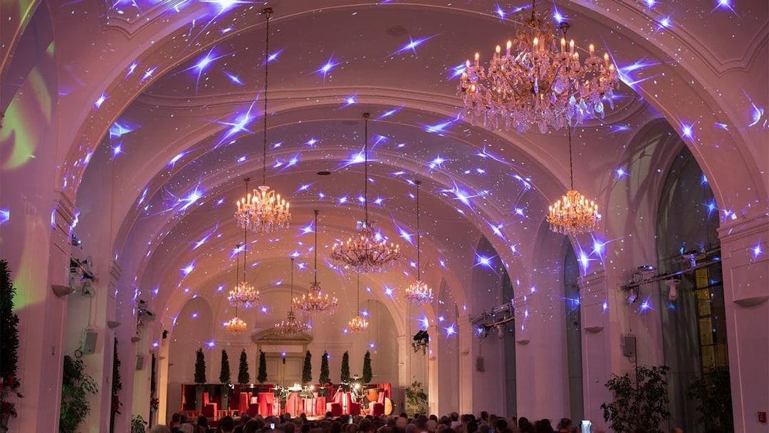 Concert audience in Schönbrunn Palace hall with chandeliers and starry light display.