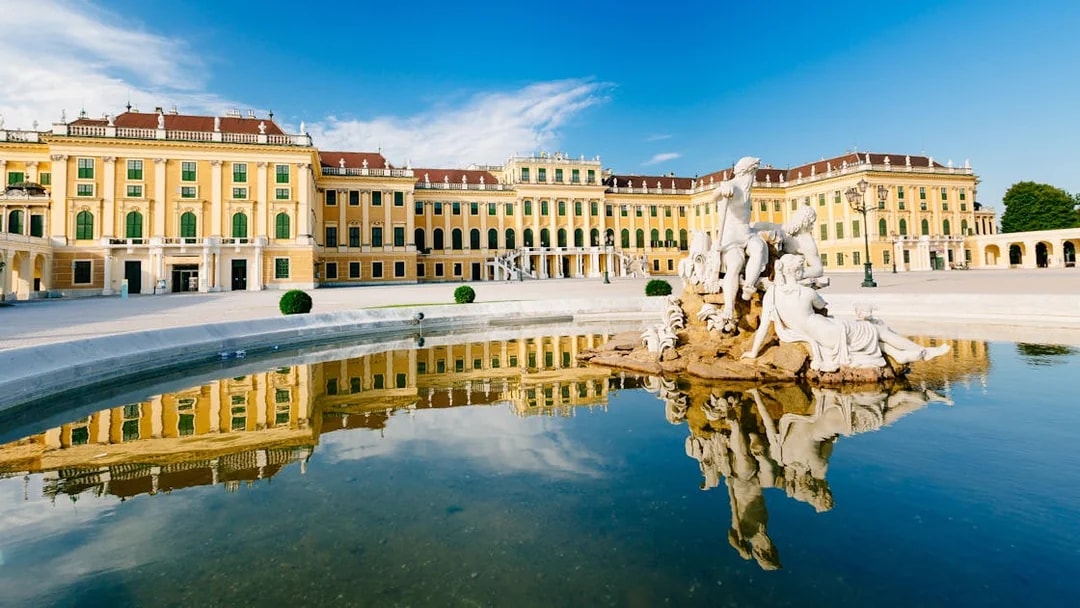 Schönbrunn Palace with Neptune Fountain in Vienna, Austria, reflecting in water.