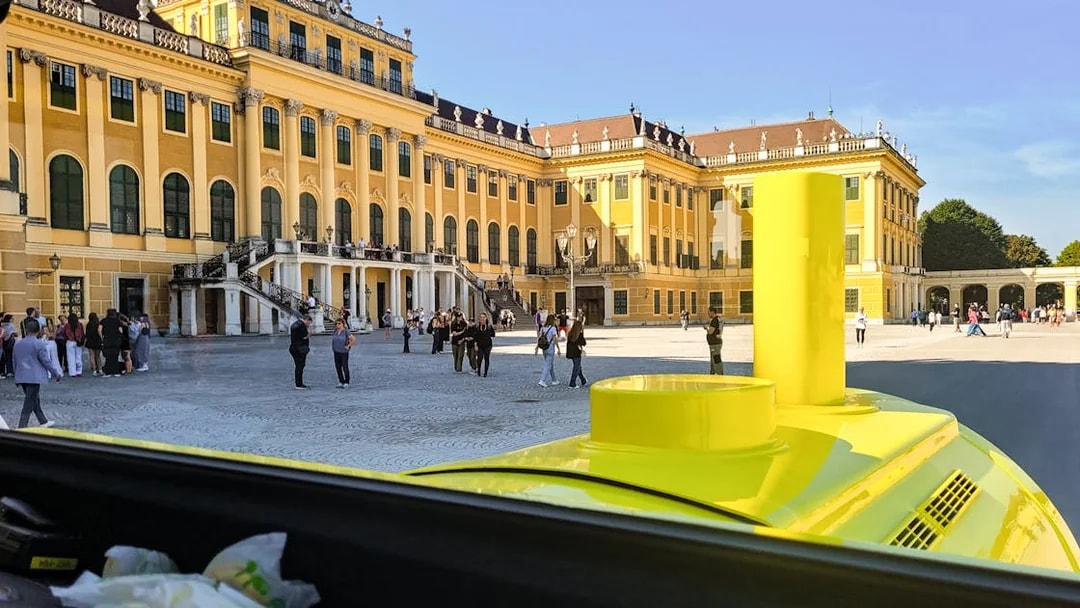 Panorama Train view of Schönbrunn Palace courtyard, Vienna, with visitors exploring.