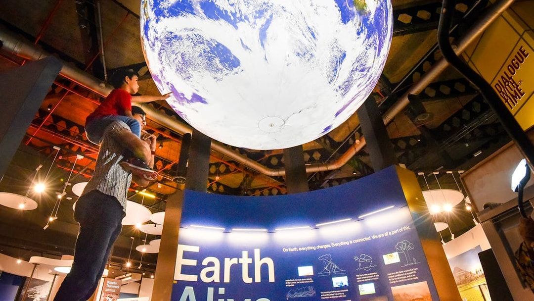Child on adult's shoulders reaching for Earth exhibit at Science Centre Singapore.