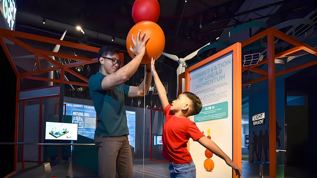 Child and adult interacting with a physics exhibit at Science Centre Singapore.