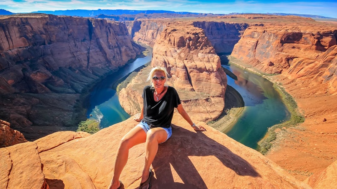 Horseshoe Bend view with person sitting on rock, part of Secret Antelope Canyon tour.