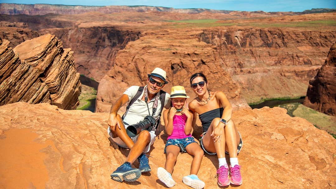 Family sitting on red rock cliff at Horseshoe Bend, Arizona, during Secret Antelope Canyon tour.