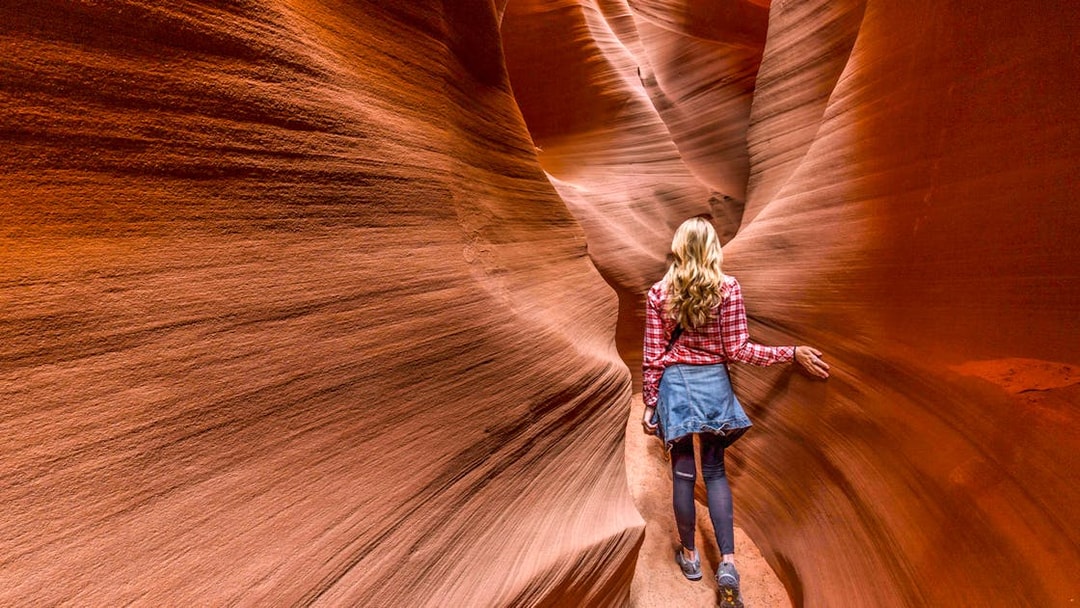Person walking through narrow sandstone walls in Secret Antelope Canyon.