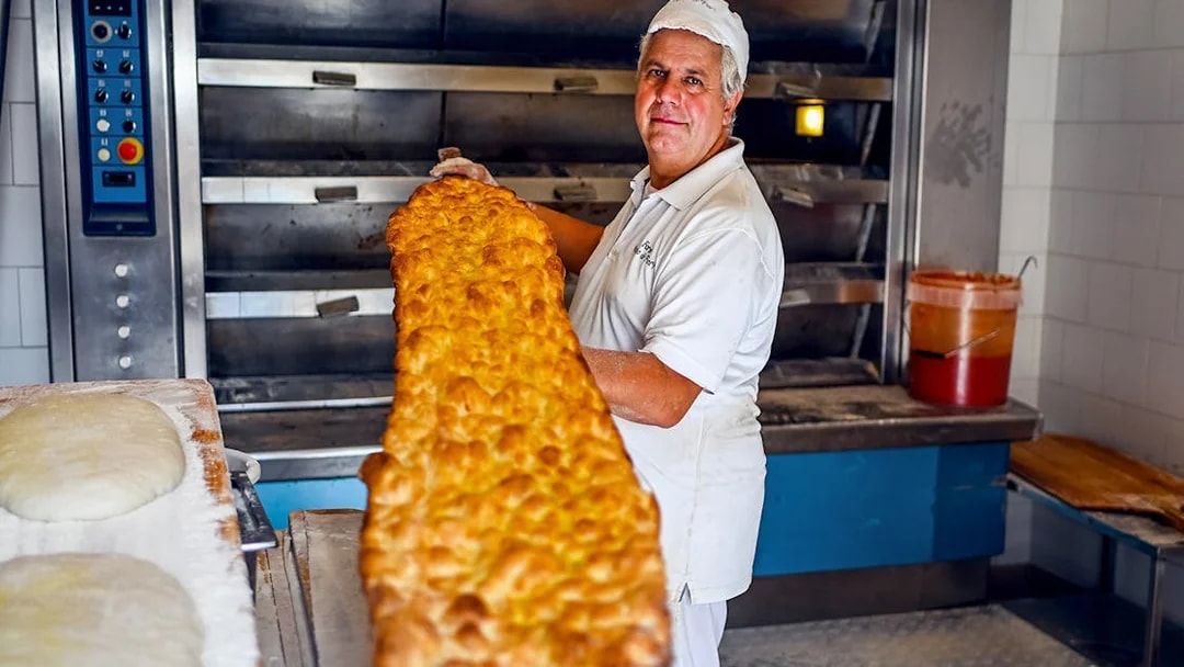 Baker holding large pizza in Rome bakery during food tour.
