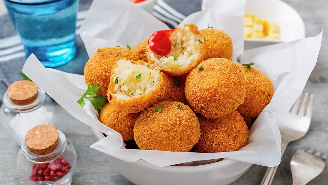 Risotto balls with crispy coating in a bowl, garnished with herbs.
