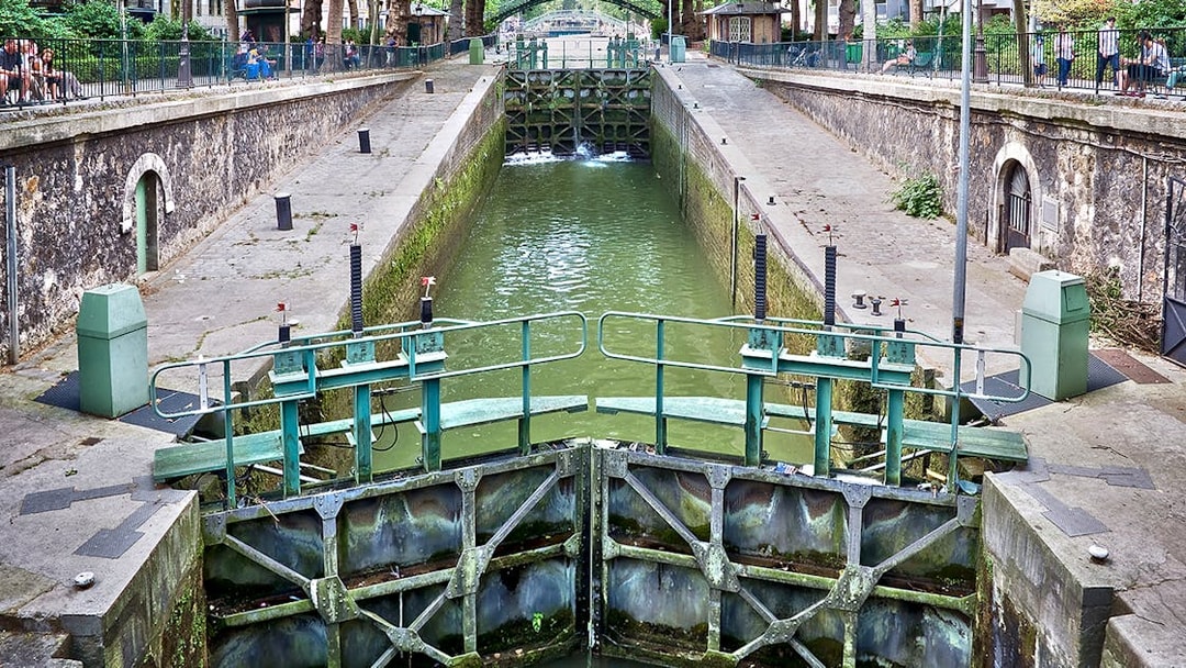 Canal lock on Canal Saint-Martin in Paris, France, with surrounding walkways and greenery.