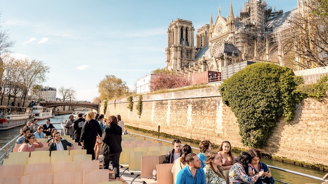 Seine River cruise with tourists near Notre-Dame Cathedral in Paris.