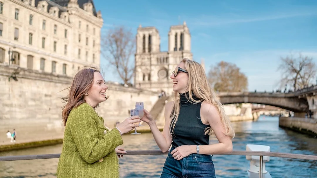 People enjoying champagne on a Seine River cruise with Notre-Dame Cathedral in the background.
