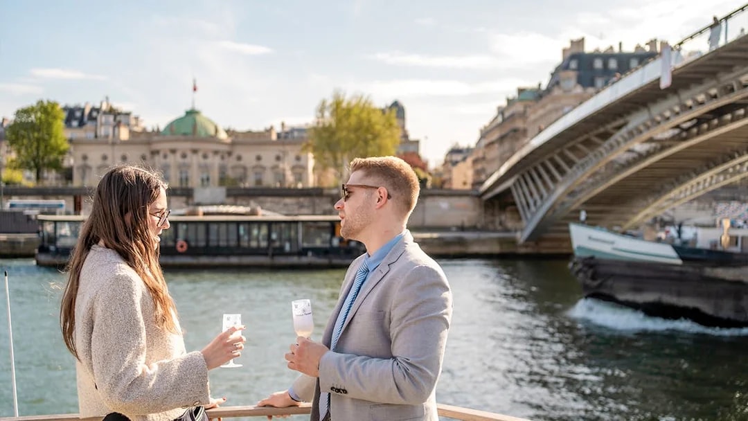 People enjoying champagne on a Seine River cruise in Paris with a bridge in the background.